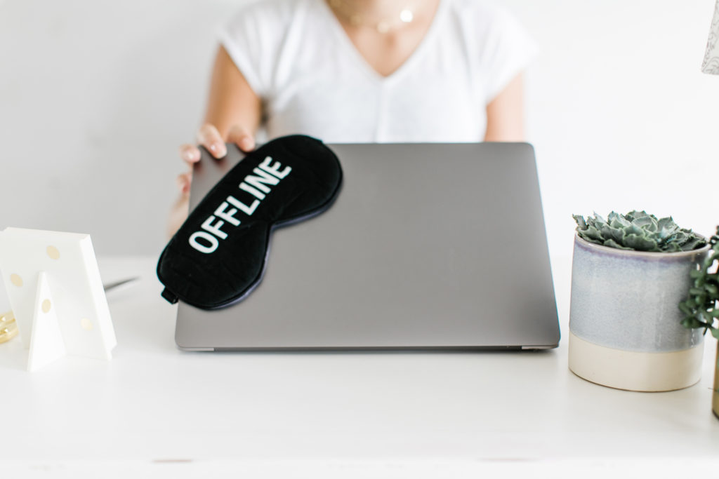 woman closing laptop with a sleeping mask on it that says offline to help reduce anxiety